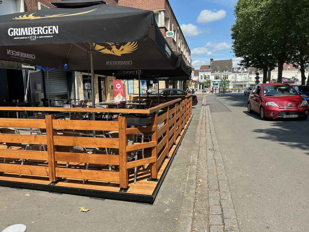 Terrasse en bois de la Brasserie de la Place avec des parasols Grimbergen