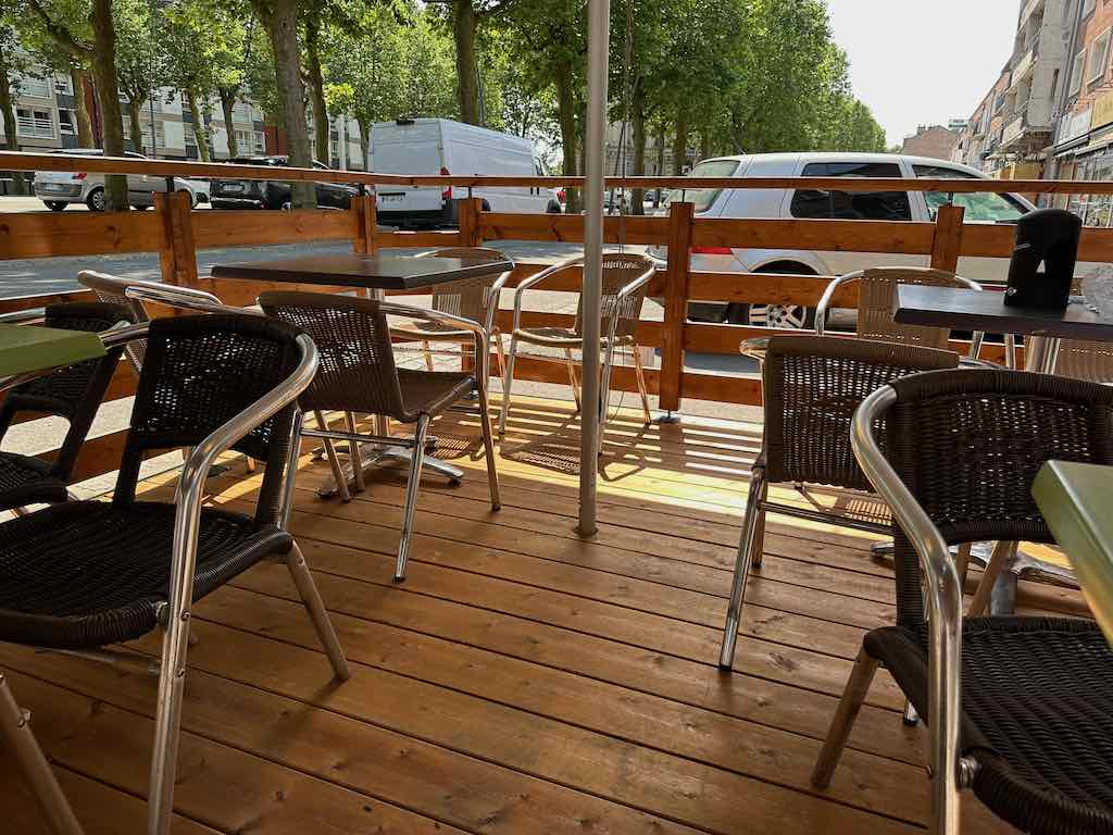 Vue intérieure d’une terrasse en bois avec des tables et des chaises en osier et métal