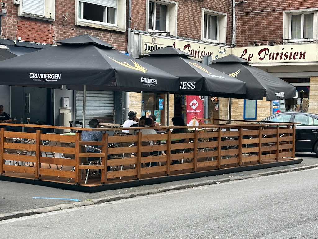 Terrasse urbaine en bois devant le café Le Parisien, équipée de parasols Grimbergen et Guinness