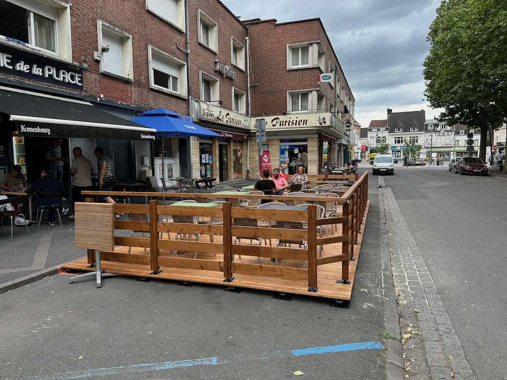 Terrasse en bois de la Brasserie de la Place avec des clients assis autour de tables en plein air