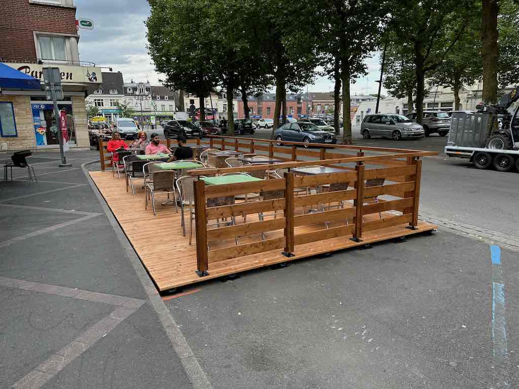 Terrasse en bois de la Brasserie de la Place avec des clients assis autour de tables en plein air