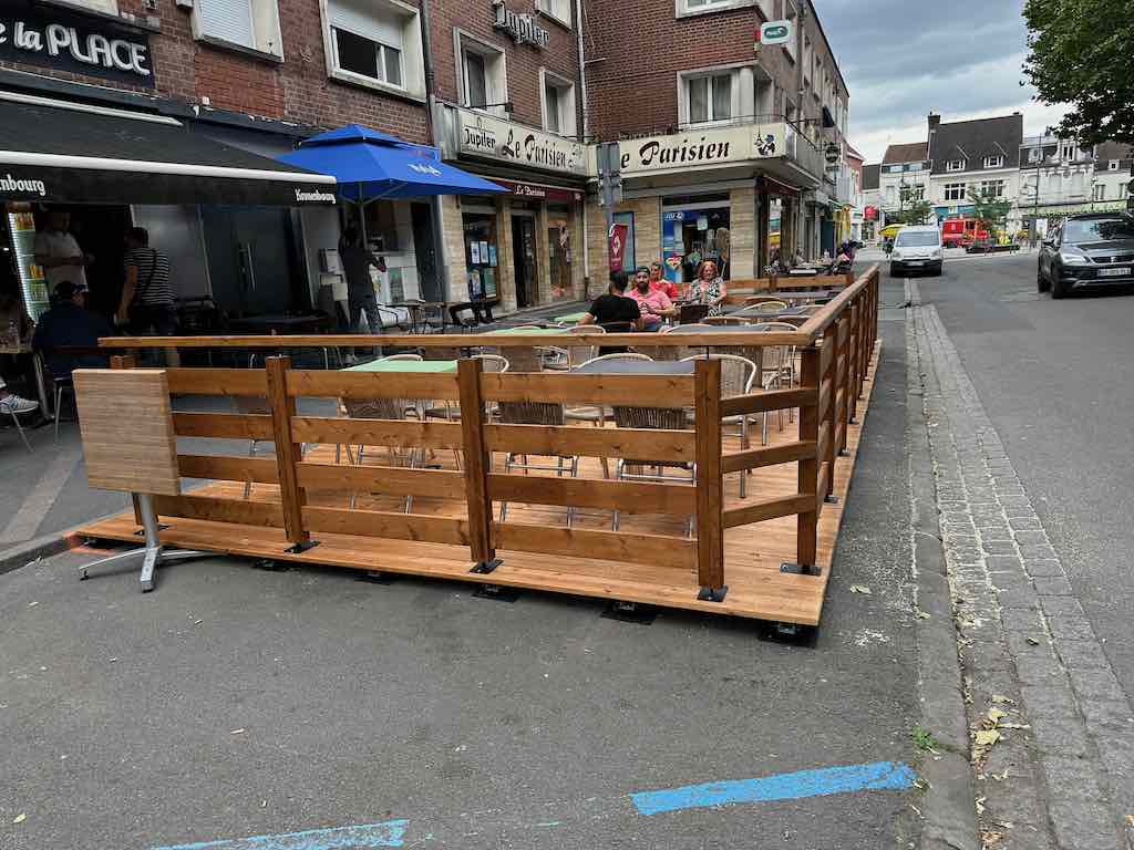 Terrasse en bois de la Brasserie de la Place avec des clients assis autour de tables en plein air